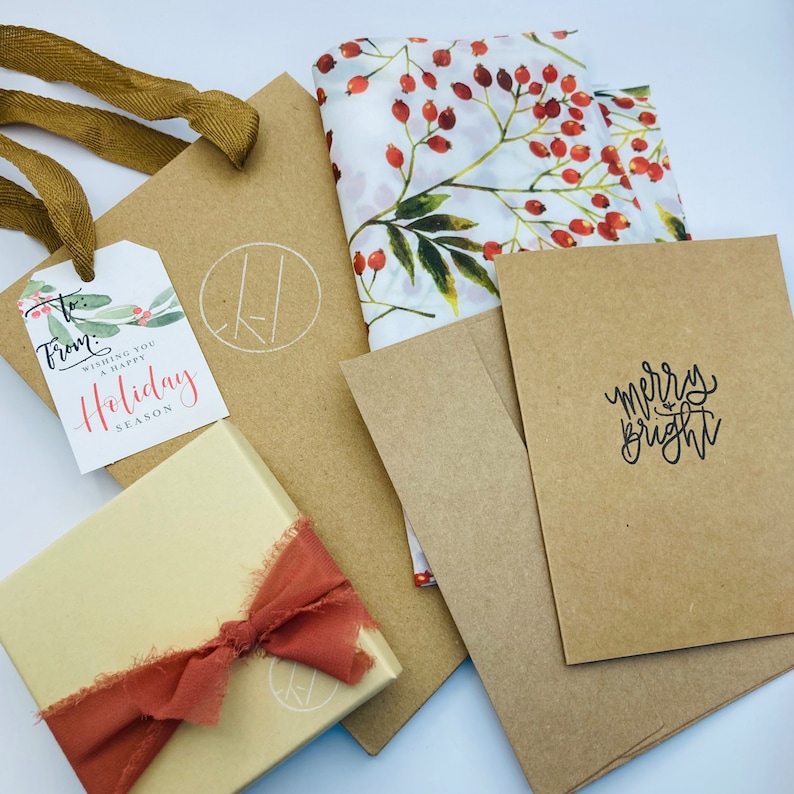 May include: A brown paper gift bag with a white tag that says "From: Wishing you a Happy Holiday Season". The bag is decorated with a brown ribbon and a white floral patterned fabric. There is also a brown card with the text "Merry Bright" on it.