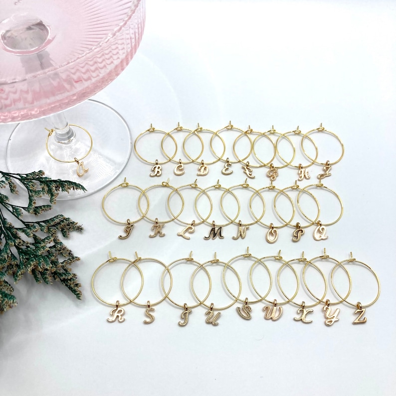 May include: Set of 26 gold-tone metal wine glass charms with letter charms from A to Z.