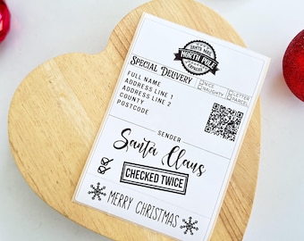 Op de afbeelding: Een wit kerstlabel met de tekst "Santa Mail North Pole Express" en "Special Delivery". Het label bevat velden voor adresinformatie en een QR-code. De afzender is "Santa Claus", met "Checked Twice" en "Merry Christmas" afgedrukt.