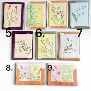 May include: A collection of nine sets of botanical greeting cards, numbered one through nine, each featuring unique floral illustrations in various colors, packaged in individual paper sleeves with deckled edges and visible artist signatures.