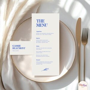 Peut inclure: Un menu de mariage et une carte de table avec du texte bleu sur fond blanc. Le menu indique "THE MENU" et répertorie les entrées, les plats, les plats principaux et le dessert. La carte de table indique "CASSIE BEAUMONT, TABLE ELEVEN."