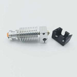 May include: A silver-colored 3D printer hot end with a ribbed heat sink, a brass nozzle, and an orange accent. A black plastic part sits next to the hot end. The components are on a white background.
