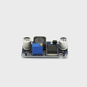 May include: A small, rectangular blue circuit board with various electronic components. It features two cylindrical capacitors, a black inductor, a blue potentiometer, and a black integrated circuit. The board is designed for electronic projects and DIY enthusiasts.