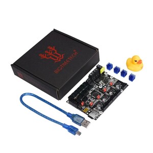Puede incluir: Una placa de circuito negra con componentes rojos y plateados, un cable USB azul y una caja negra con el texto "BIGTREETECH" en rojo. También se incluyen disipadores de calor azules y un patito de goma amarillo.