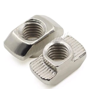 May include: Two silver-colored T-nuts with threaded holes. One nut is in focus, showing a detailed view of the threads. The nuts have a rectangular shape with beveled edges and a textured surface on one side.
