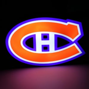 May include: A glowing sign featuring the Montreal Canadiens logo. The logo is a stylized "C" with an "H" inside, in orange with a white outline and a blue border. The background is black.