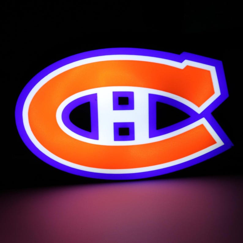 May include: A glowing sign featuring the Montreal Canadiens logo. The logo is a stylized "C" with an "H" inside, in orange with a white outline and a blue border. The background is black.