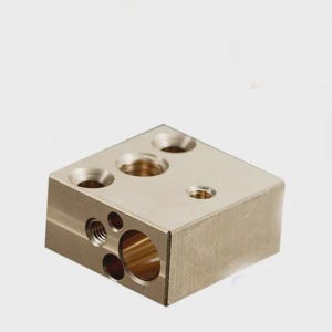 May include: A metallic gold-colored, cube-shaped component with multiple drilled holes of varying sizes. The component has a smooth, reflective surface and appears to be made of metal. The holes are precisely drilled, suggesting a mechanical or industrial application.