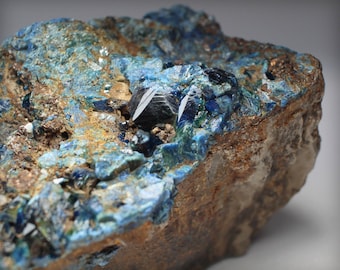 May include: A close-up of a rough, brown rock with a cluster of blue and green crystals. The crystals are sharp and have a metallic sheen.