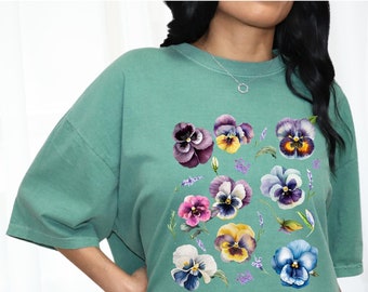May include: A teal green oversized t-shirt with a watercolor print of purple, yellow, and white pansies.