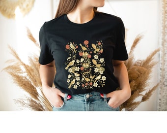 May include: Black t-shirt with a floral design featuring birds and flowers in shades of yellow, orange, and green.