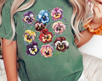 May include: A green t-shirt with a floral print of colorful pansies. The pansies are arranged in a cluster and have a watercolor effect.