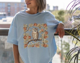 May include: A light blue t-shirt with a graphic of an owl perched on a branch surrounded by flowers. The owl is brown and white with yellow eyes.