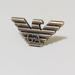 May include: A silver-toned metal eagle with the letters "GA" in the center. The eagle has a textured, striped design.