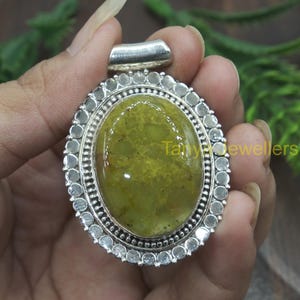 May include: A silver pendant featuring a green opal stone set within a silver frame. The frame is adorned with a row of small silver beads.