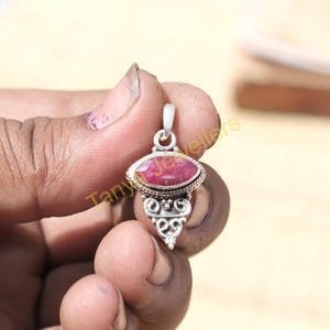 May include: A silver pendant featuring a red gemstone set in a silver oval bezel. The pendant has a decorative silver design below the gemstone.