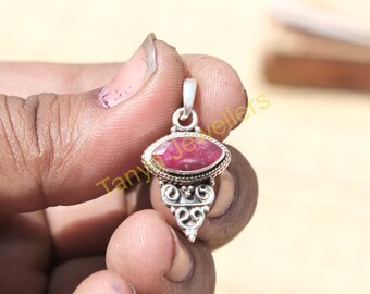 May include: A silver pendant featuring a red gemstone set in a silver oval bezel. The pendant has a decorative silver design below the gemstone.