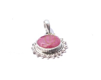May include: A silver pendant with a large, oval ruby gemstone. The ruby is a bright red hue, set in a decorative silver bezel with a floral design around the edge. The pendant has a silver bail for attaching to a chain. The ruby is approximately 2 cm in length.