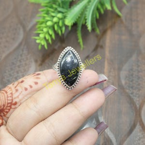 May include: A silver ring with a black and white marbled stone set in a marquise shape.