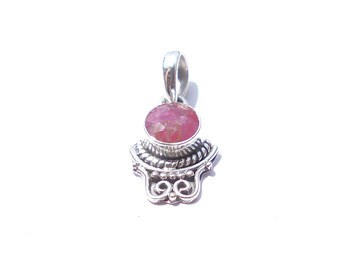 May include: A silver pendant featuring a pink gemstone. The pendant has a decorative base with a swirling design and a loop at the top for a chain. The gemstone is oval-shaped and a light pink colour.