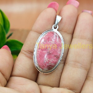 Peut inclure: Un pendentif ovale en argent avec une pierre précieuse rose et blanche. Le pendentif a une bordure argentée détaillée.