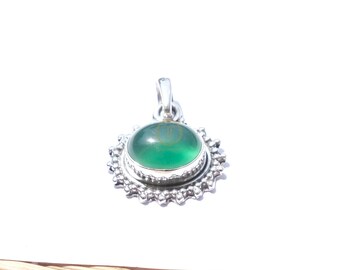 May include: A silver pendant with a round, bright green gemstone. The gemstone is set in a detailed, ornate silver setting with a sunburst design. The pendant has a small loop for a chain.