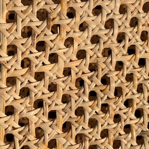 May include: Close-up of a woven rattan material. The natural-toned material is intricately woven in a repeating pattern, creating a textured surface. The weave allows light and shadow to play across the surface, highlighting the detailed craftsmanship.