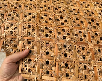 May include: Close-up of a section of woven rattan material. The natural-toned material is constructed in a repeating pattern of squares and rectangles, with small circular openings. The texture is visible, showing the individual strands of the material.