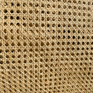 May include: Close-up of a woven rattan material with a repeating geometric pattern. The natural-toned material has a textured surface with small, evenly spaced holes. The weave creates a grid-like design, ideal for furniture or decorative applications.