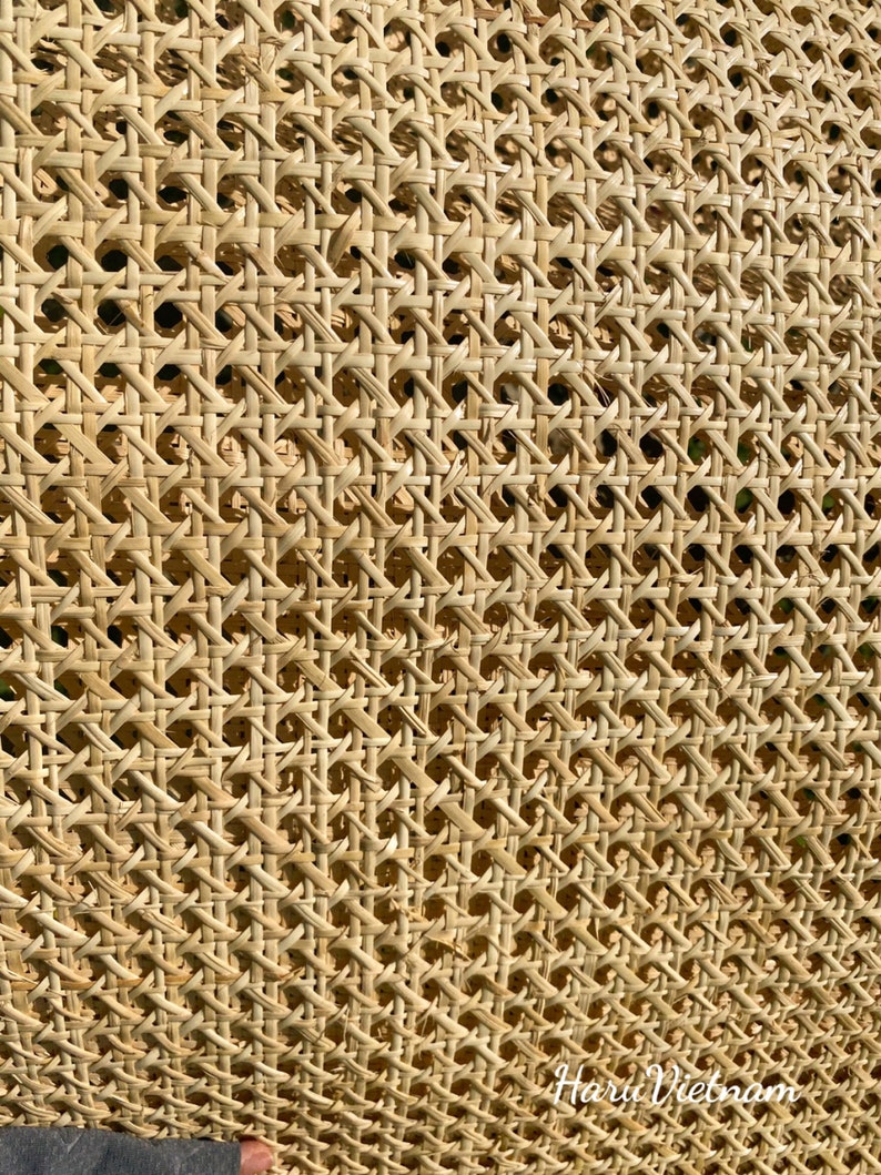 May include: Close-up of a woven rattan material with a repeating geometric pattern. The natural-toned material has a textured surface with small, evenly spaced holes. The weave creates a grid-like design, ideal for furniture or decorative applications.