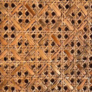 May include: Close-up of a woven rattan texture. The natural material is a light brown colour, with a repeating pattern of interwoven strips creating a grid-like design. The texture has a rustic, handcrafted appearance.