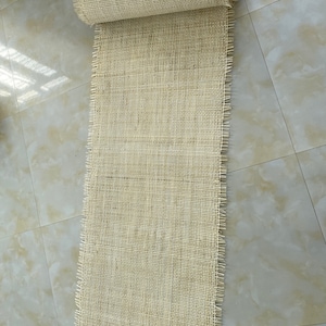 Pode incluir: Um rolo de tecido de malha de fibra natural com uma textura tecida. O tecido &eacute; bege e tem uma borda desfiada.