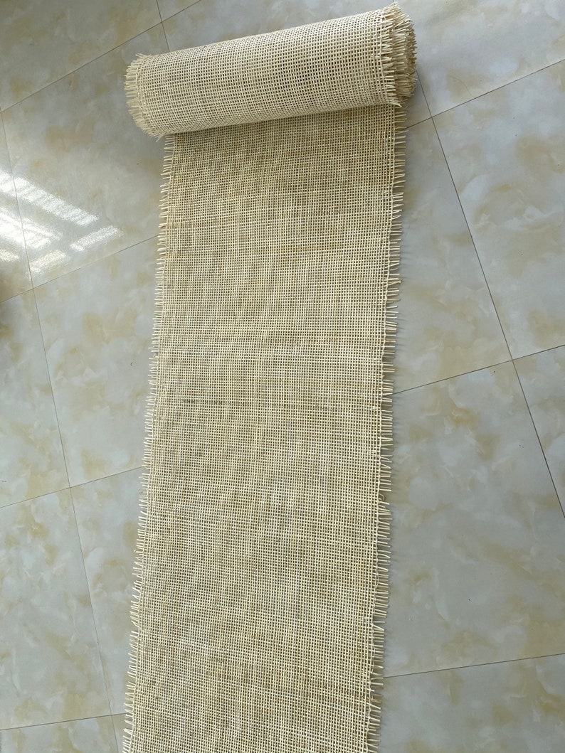 Pode incluir: Um rolo de tecido de malha de fibra natural com uma textura tecida. O tecido &eacute; bege e tem uma borda desfiada.