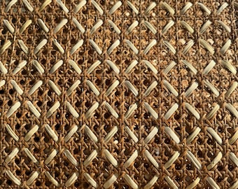 Könnte beinhalten: Nahaufnahme eines gewebten Rattanmaterials mit einem sich wiederholenden Rautenmuster. Die Naturfasern sind eine Mischung aus hellbeige und mittelbraun und erzeugen eine strukturierte Oberfläche. Dieses Material wird oft in Möbeln und Wohnaccessoires verwendet.