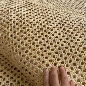 May include: A roll of natural-colored cane webbing with a woven pattern. The webbing is made of thin, light-brown strands, creating a grid-like design. The texture appears smooth and flexible, suitable for various craft projects.