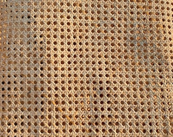 May include: Close-up of a woven cane material with a repeating pattern of small, evenly spaced holes. The natural-colored cane is tightly woven, creating a textured surface. The material is likely used for furniture or decorative purposes.