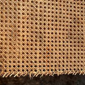 May include: Close-up of a woven cane material with a repeating pattern of small, evenly spaced holes. The natural-colored cane is tightly woven, creating a textured surface. The edges show the unfinished ends of the cane.