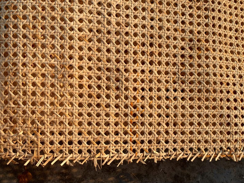May include: Close-up of a woven cane material with a repeating pattern of small, evenly spaced holes. The natural-colored cane is tightly woven, creating a textured surface. The edges show the unfinished ends of the cane.