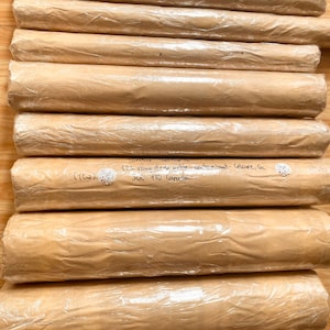 May include: A stack of brown paper tubes wrapped in clear plastic. The tubes are labeled with handwritten text, including "126 vana dada antice-cathore sout- C&eacute;saire, Ge" and "JUL ITU Caraba".