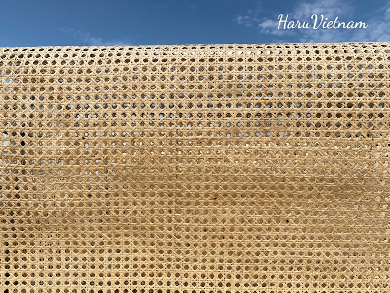 May include: Close-up of a woven rattan material with a repeating geometric pattern. The natural-colored material is tightly woven, creating a textured surface. The background is a clear blue sky with the text "Haru Vietnam".
