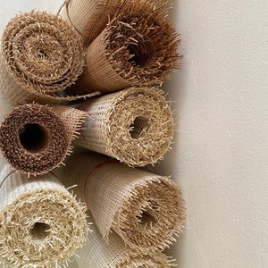 Pode incluir: Close-up de sete rolos de tecido de cana de fibra natural, um material usado para assentos de cadeiras e outras tape&ccedil;arias de m&oacute;veis. Os rolos est&atilde;o empilhados verticalmente, com o rolo superior parcialmente obscurecido pelos outros. Os rolos s&atilde;o de diferentes tamanhos e t&ecirc;m uma textura natural tecida.