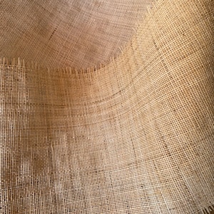 May include: A close-up of a natural brown burlap fabric with a woven texture. The fabric is folded and has a frayed edge.