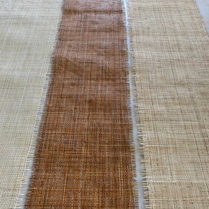 May include: Three strips of woven fabric, one brown, one white, and one beige, laid out side by side. The fabric has a woven texture and is likely used for crafting.