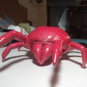 Peut inclure: Modèle de plastique rouge détaillé d'une araignée à huit pattes. L'araignée est posée avec ses pattes tendues et sa tête face à l'appareil photo.