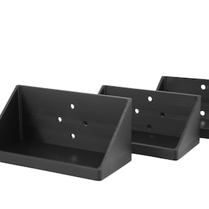 Op de afbeelding: Drie zwarte hoekplanken van plastic, elk 17 cm lang. De planken hebben een driehoekige vorm en zijn ontworpen om aan de muur te worden gemonteerd.