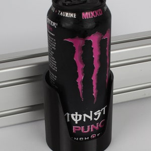May include: A black can holder with a Monster Energy drink can inside. The can is black with pink Monster claws and the text "Monster Punch" on the front.