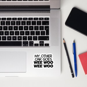 May include: A black and white sticker with the text "My other car goes wee woo wee woo" on a white laptop.