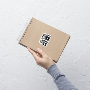 May include: A brown notebook with a spiral binding and a sticker that says "My other car goes wee woo wee woo".