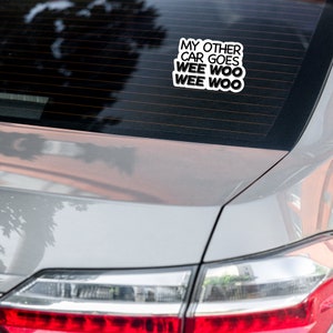 May include: A white car with a sticker on the back window that says "My other car goes wee woo wee woo".