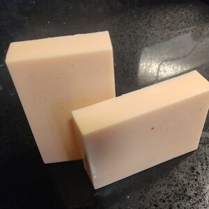 May include: Two rectangular bars of pale peach-coloured soap. The bars are slightly different sizes and have a speckled appearance.